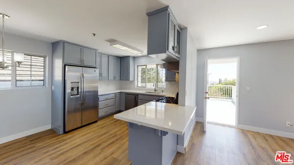 a kitchen with stainless steel appliances granite countertop a refrigerator a sink dishwasher a stove and white countertops with wooden floor