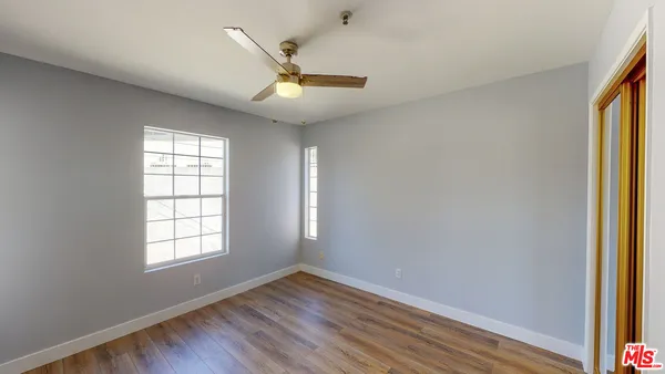 an empty room with wooden floor fan and windows