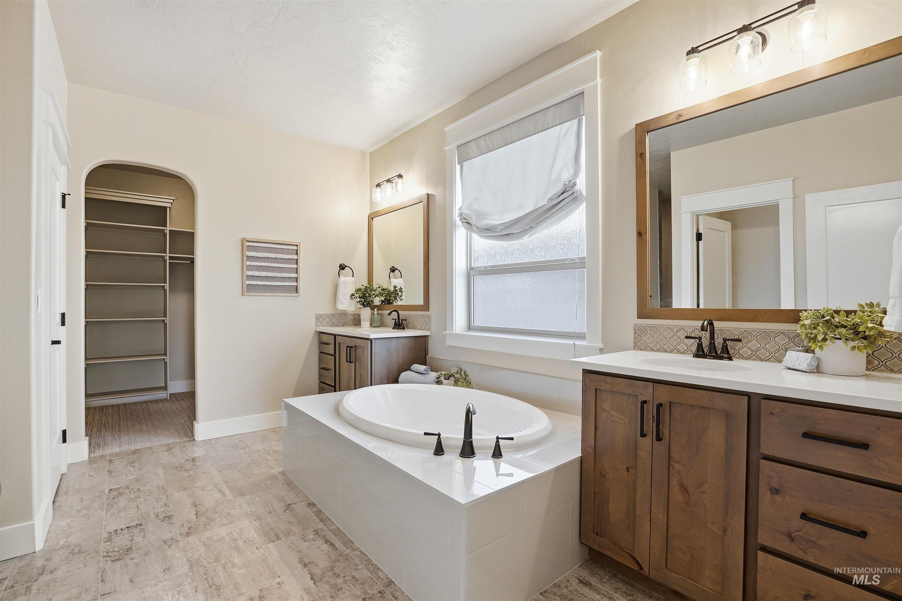 3915 West Riva Capri Street Meridian, ID 83646 - Photo 21 of 49 Freestanding soaking tub with matte black fixtures, dual wood-finish vanities with white countertops, decorative tile backsplashes, and large framed mirrors