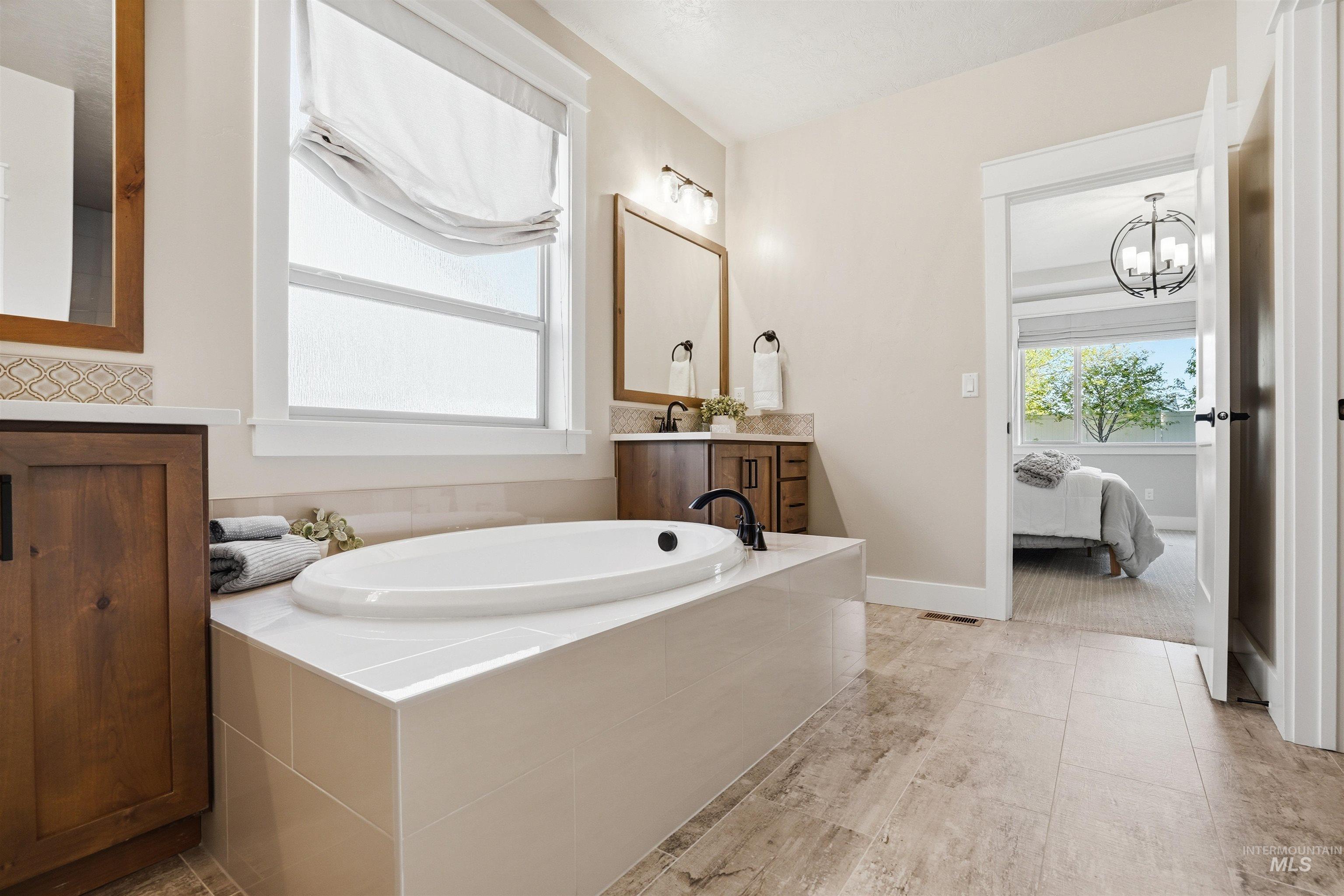 3915 West Riva Capri Street Meridian, ID 83646 - Photo 22 of 49 Soaking tub with tiled surround, wood-finish vanity with countertop, and large window with privacy shade