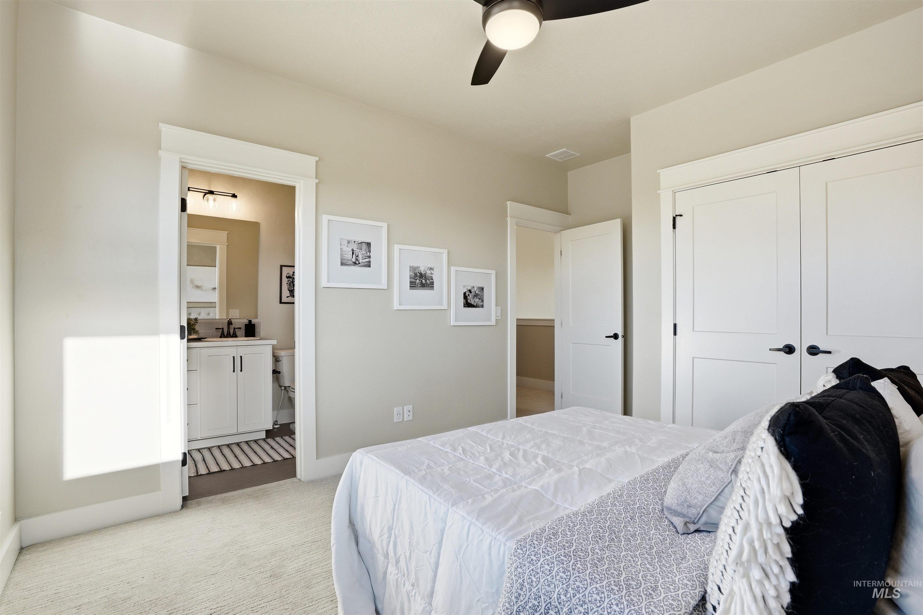 3915 West Riva Capri Street Meridian, ID 83646 - Photo 26 of 49 Carpeted bedroom with a ceiling fan, two-panel closet doors with matte black hardware, and an en-suite bathroom featuring a vanity with a white cabinet and a rectangular sink
