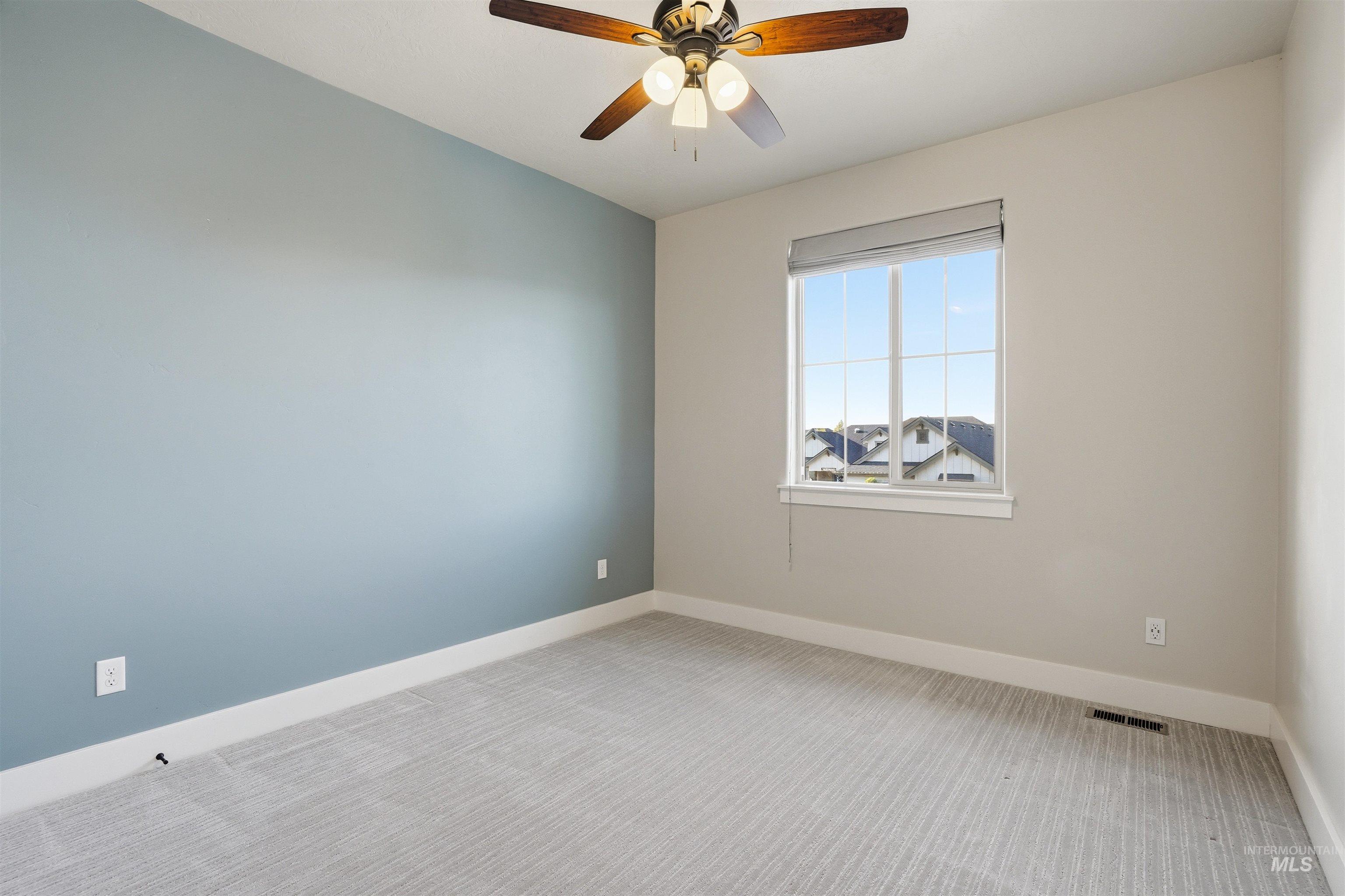 3915 West Riva Capri Street Meridian, ID 83646 - Photo 31 of 49 Room featuring textured carpet flooring, a window with a roller shade, a ceiling fan with integrated lighting, and a contrasting accent wall