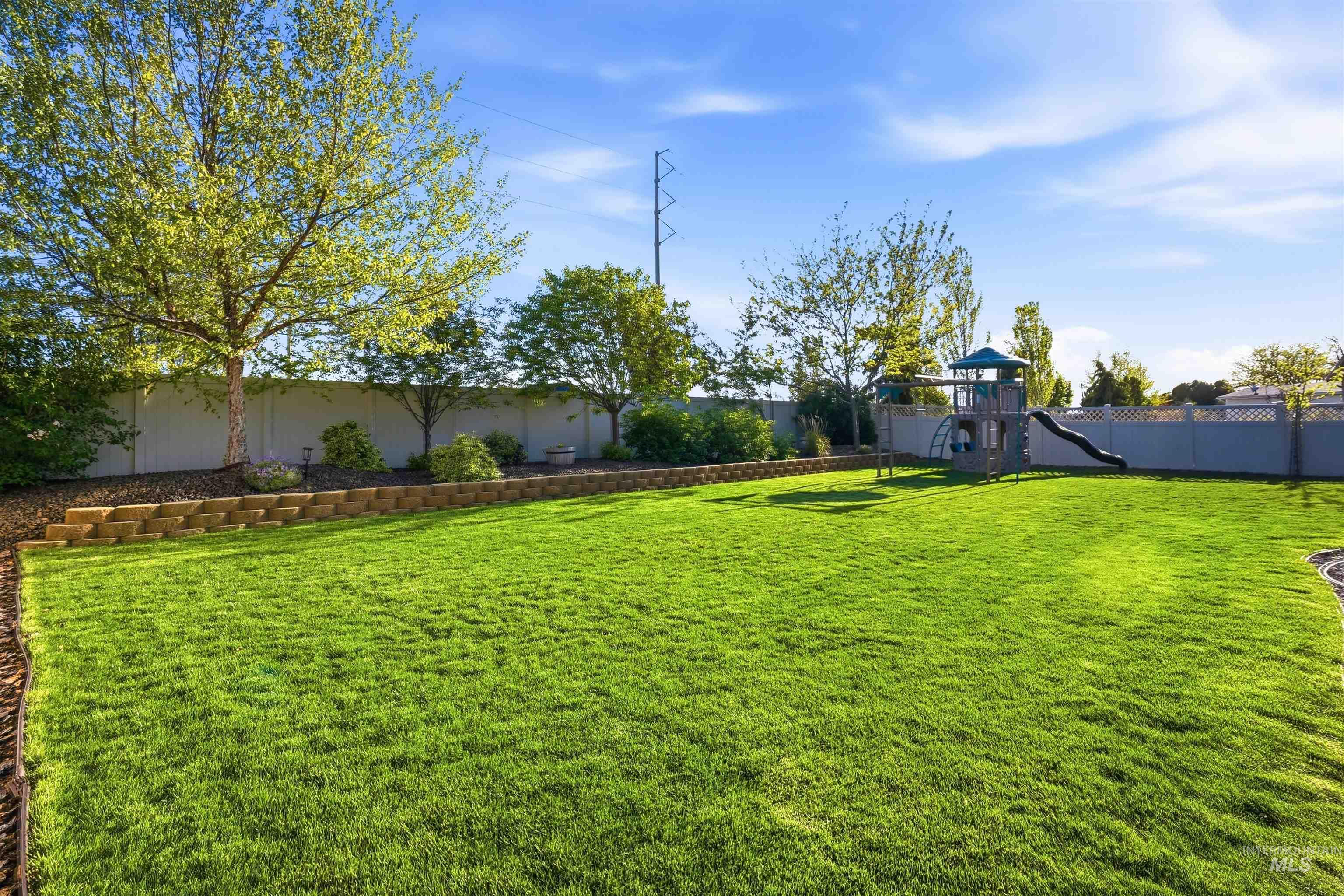 3915 West Riva Capri Street Meridian, ID 83646 - Photo 35 of 49 Expansive green lawn with mature trees and a tiered retaining wall