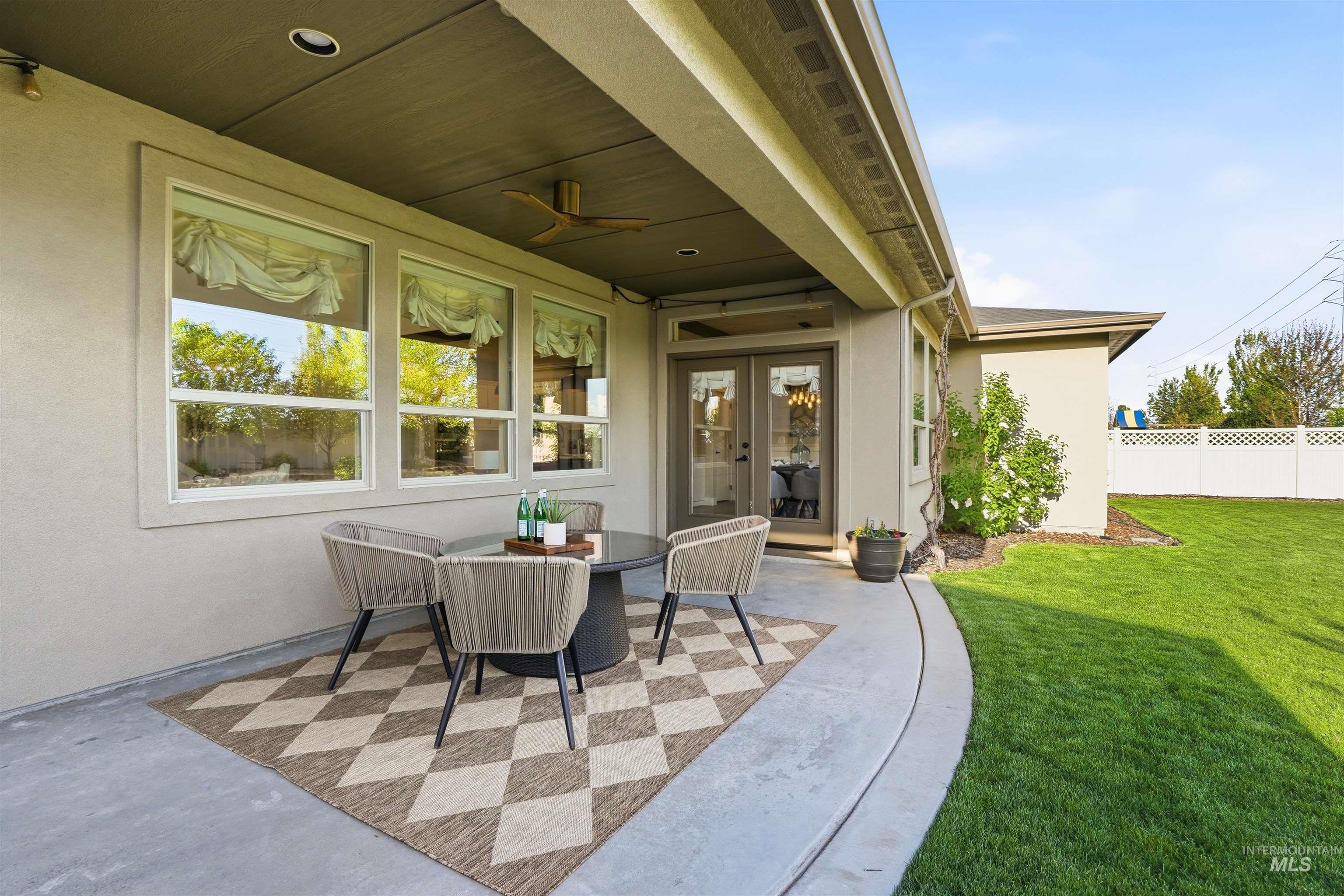 3915 West Riva Capri Street Meridian, ID 83646 - Photo 38 of 49 Covered patio featuring an outdoor ceiling fan, multiple windows, French doors, and a concrete patio extending to a manicured lawn with a white privacy fence