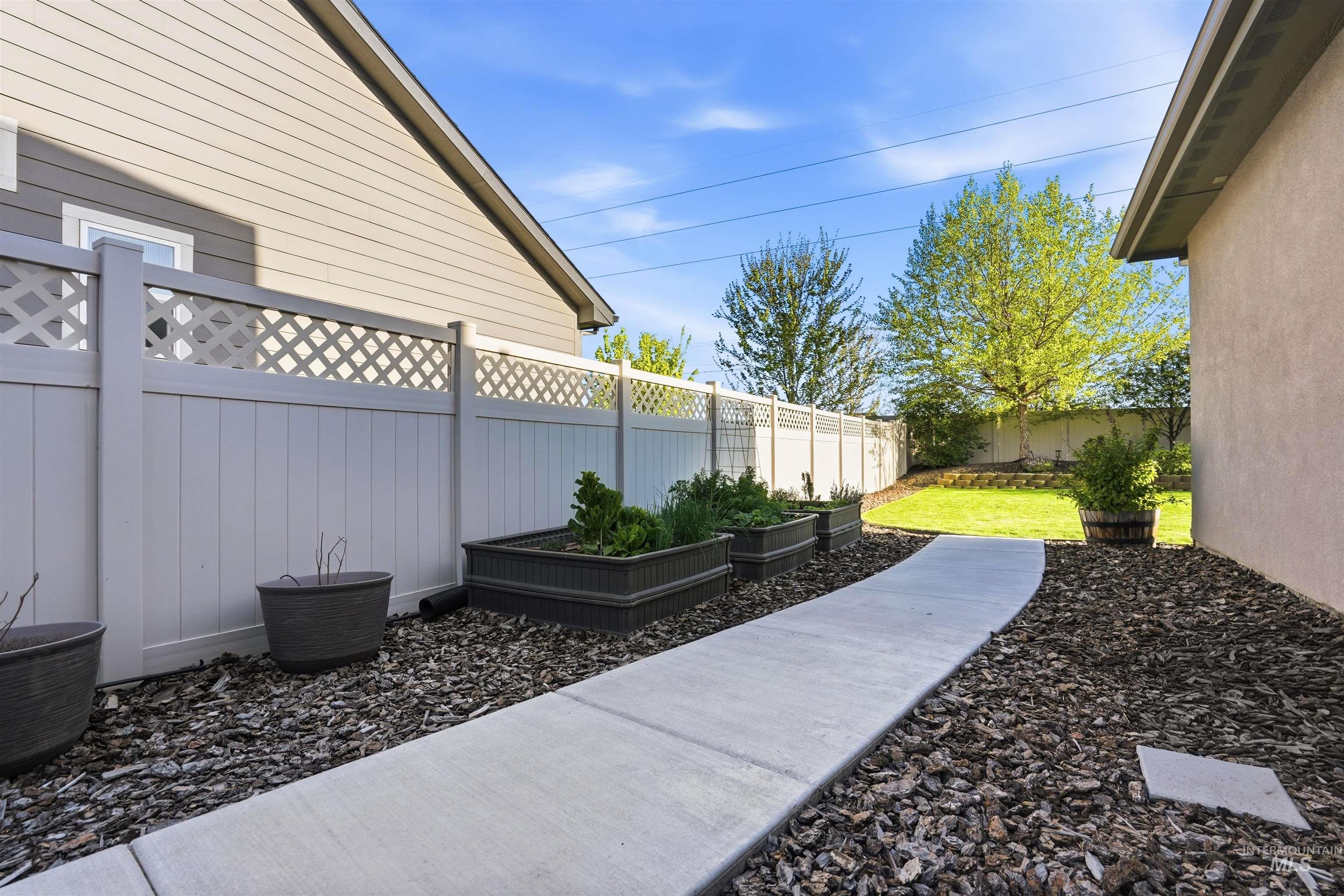3915 West Riva Capri Street Meridian, ID 83646 - Photo 39 of 49 Concrete pathway with bark landscaping featuring raised garden beds and a lattice-top privacy fence