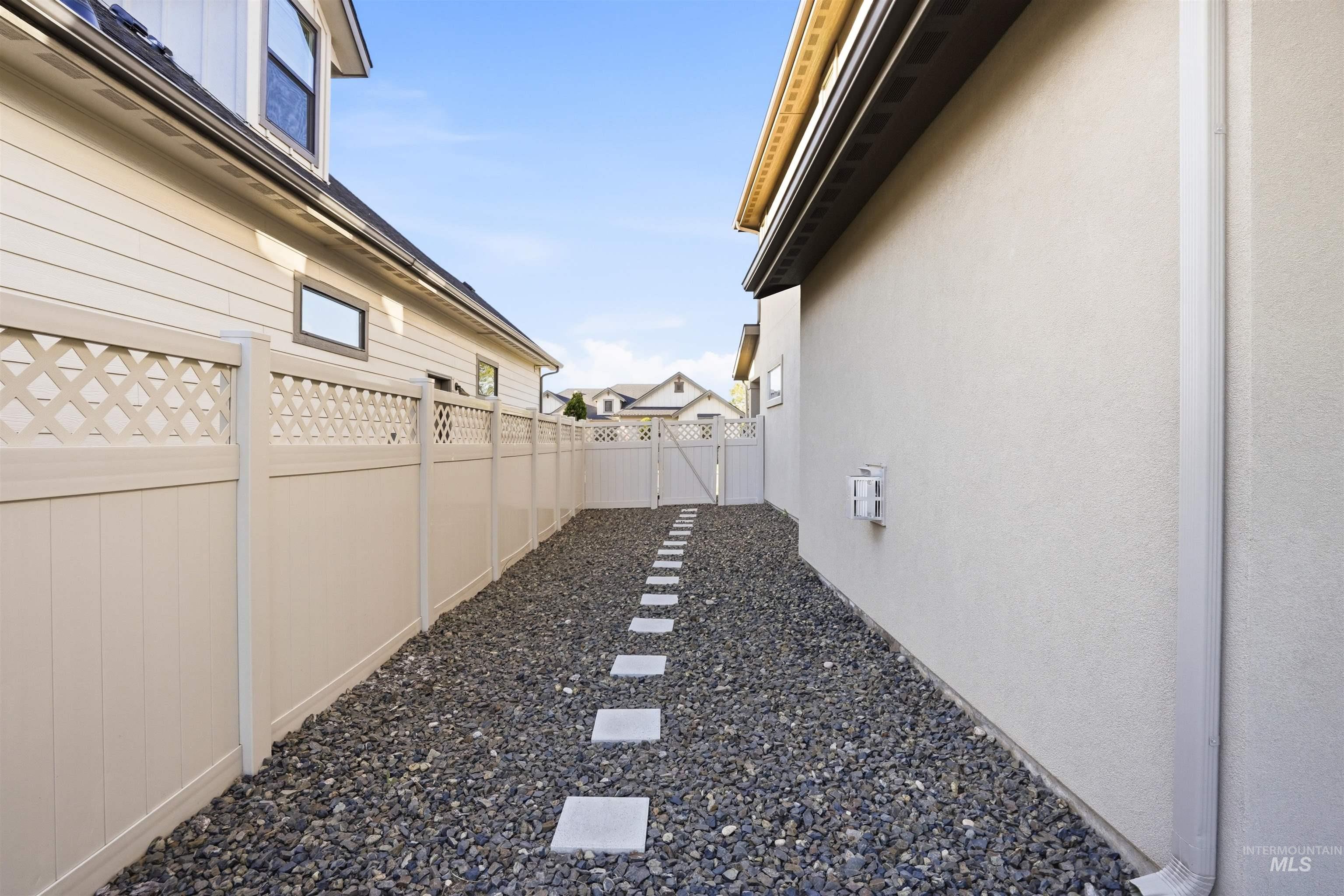 3915 West Riva Capri Street Meridian, ID 83646 - Photo 40 of 49 Side yard featuring gravel ground cover with stepping stones, a light-colored privacy fence with lattice accents, and a stucco exterior wall