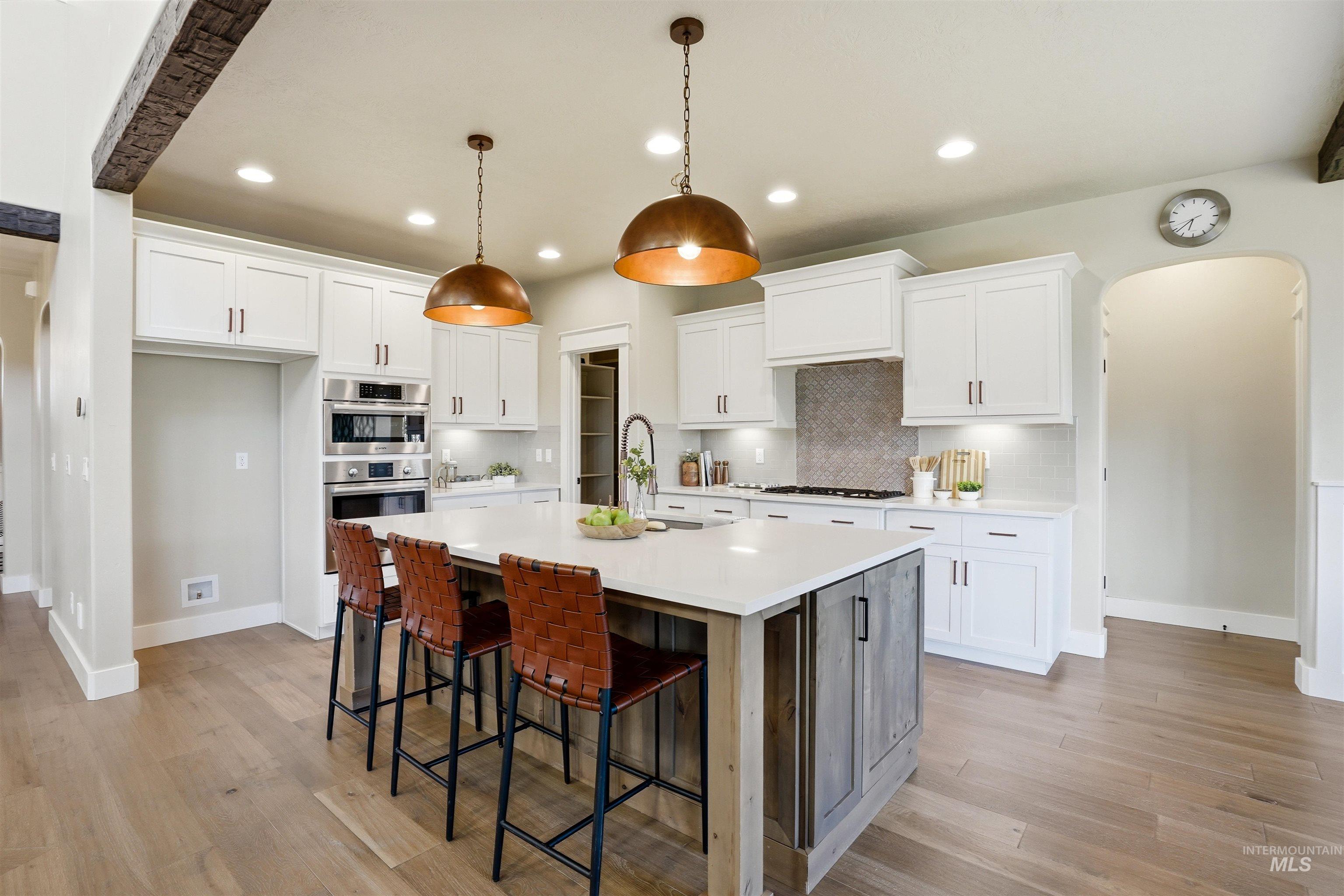 3915 West Riva Capri Street Meridian, ID 83646 - Photo 7 of 49 Spacious kitchen featuring a large central island with quartz countertop, white shaker cabinetry, stainless steel appliances, and wood-finish flooring