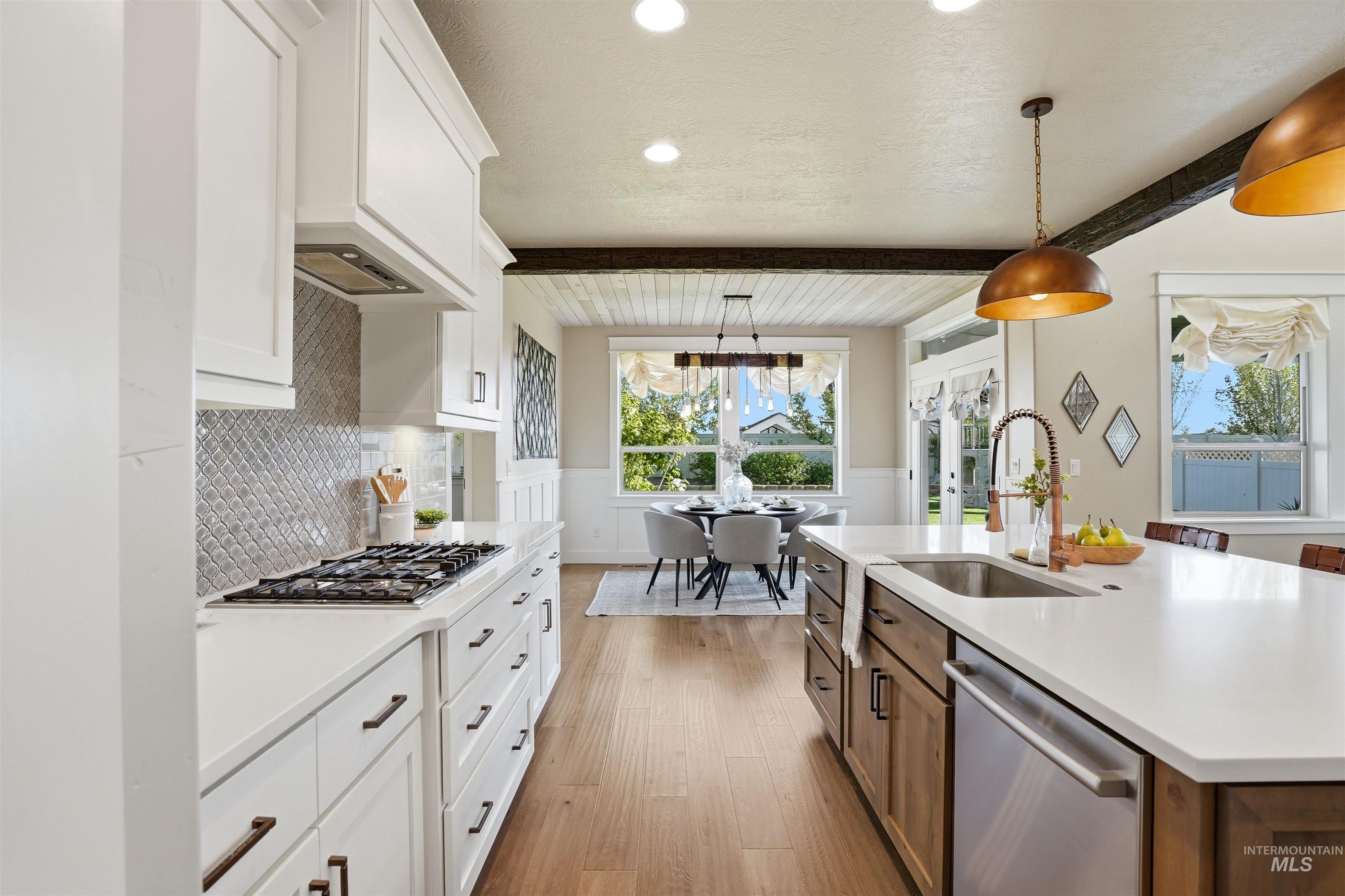 3915 West Riva Capri Street Meridian, ID 83646 - Photo 10 of 49 Open-concept kitchen featuring white shaker cabinetry, an island with an undermount sink, quartz countertops, a gas range with a tile backsplash, and wood-finish flooring