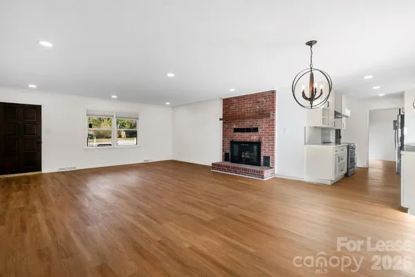 a view of a room with wooden floor ceiling fan window and a kitchen