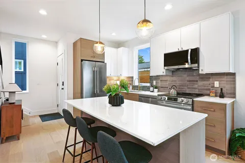 a kitchen with stainless steel appliances granite countertop a stove a refrigerator a microwave a dining table and chairs with wooden floor