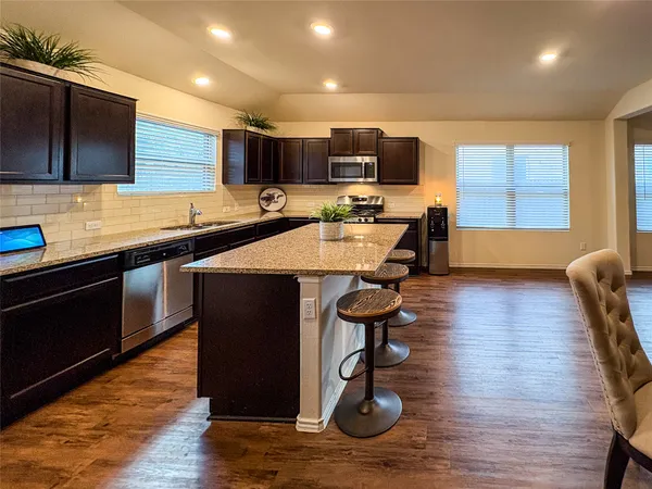 a living room with stainless steel appliances furniture wooden floor and a kitchen view