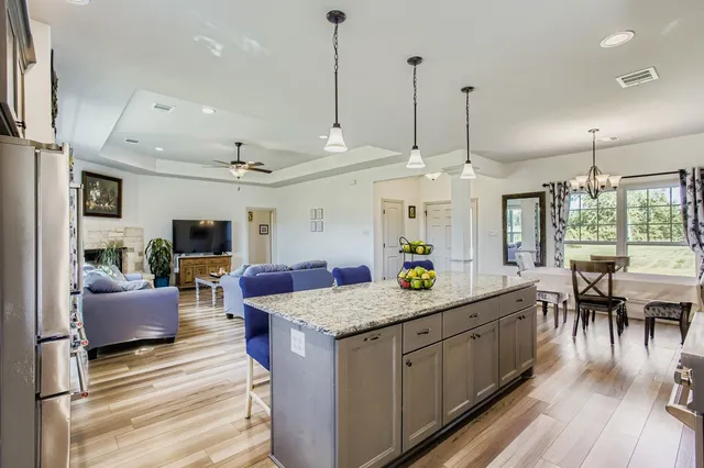 a view of living room kitchen with granite countertop stainless steel appliances refrigerator stove dining table and chairs