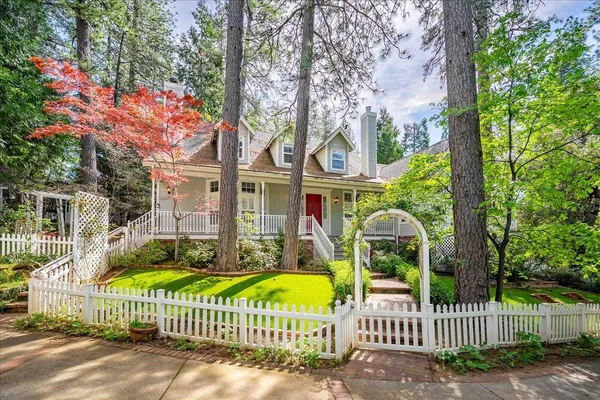 a view of a brick house with large trees and wooden fence