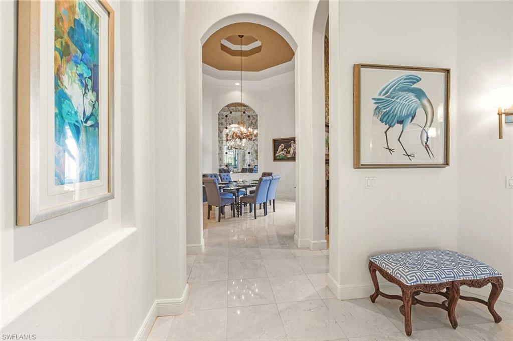 396 Terracina Way Naples, FL 34119 - Photo 11 of 50 Corridor with a tray ceiling, a chandelier, and arched walkways