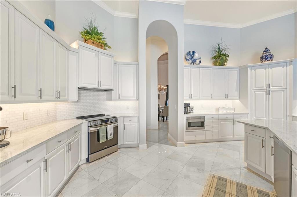 396 Terracina Way Naples, FL 34119 - Photo 18 of 50 Kitchen featuring stainless steel appliances, white cabinetry, light stone counters, crown molding, and arched walkways
