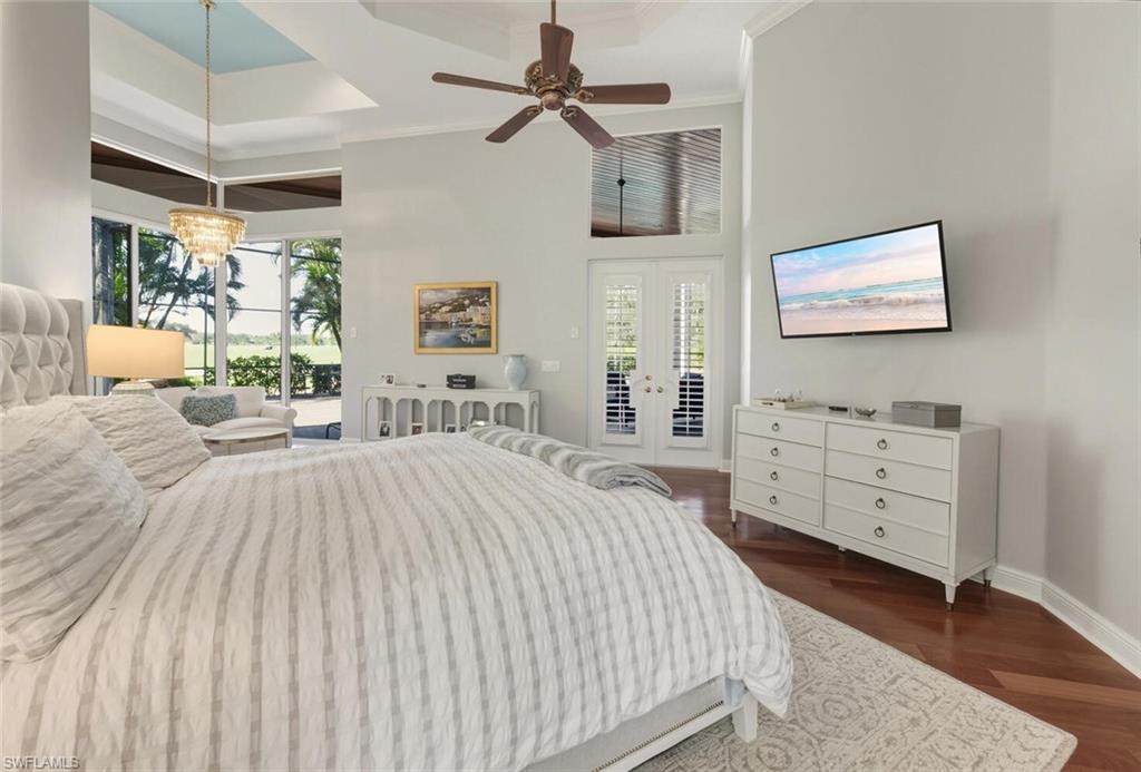 396 Terracina Way Naples, FL 34119 - Photo 31 of 50 Bedroom with access to exterior, a tray ceiling, a towering ceiling, ceiling fan, and dark wood-style floors