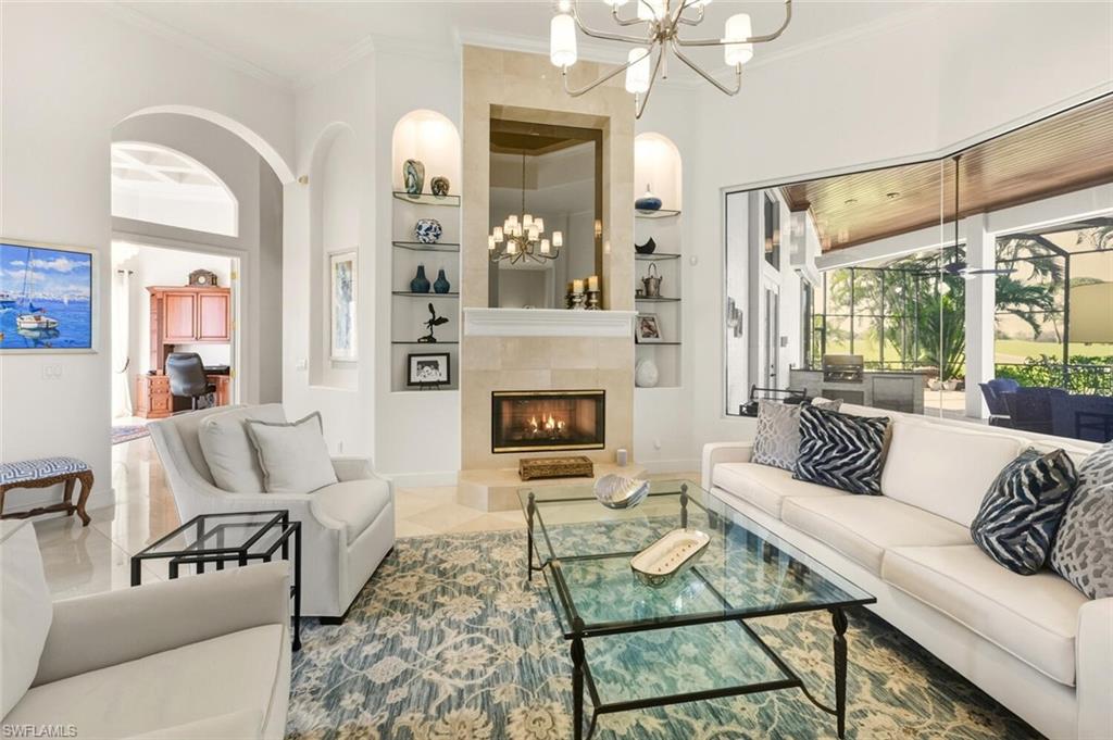 396 Terracina Way Naples, FL 34119 - Photo 10 of 50 Tiled living area featuring built in shelves, ornamental molding, a chandelier, a tiled fireplace, and arched walkways