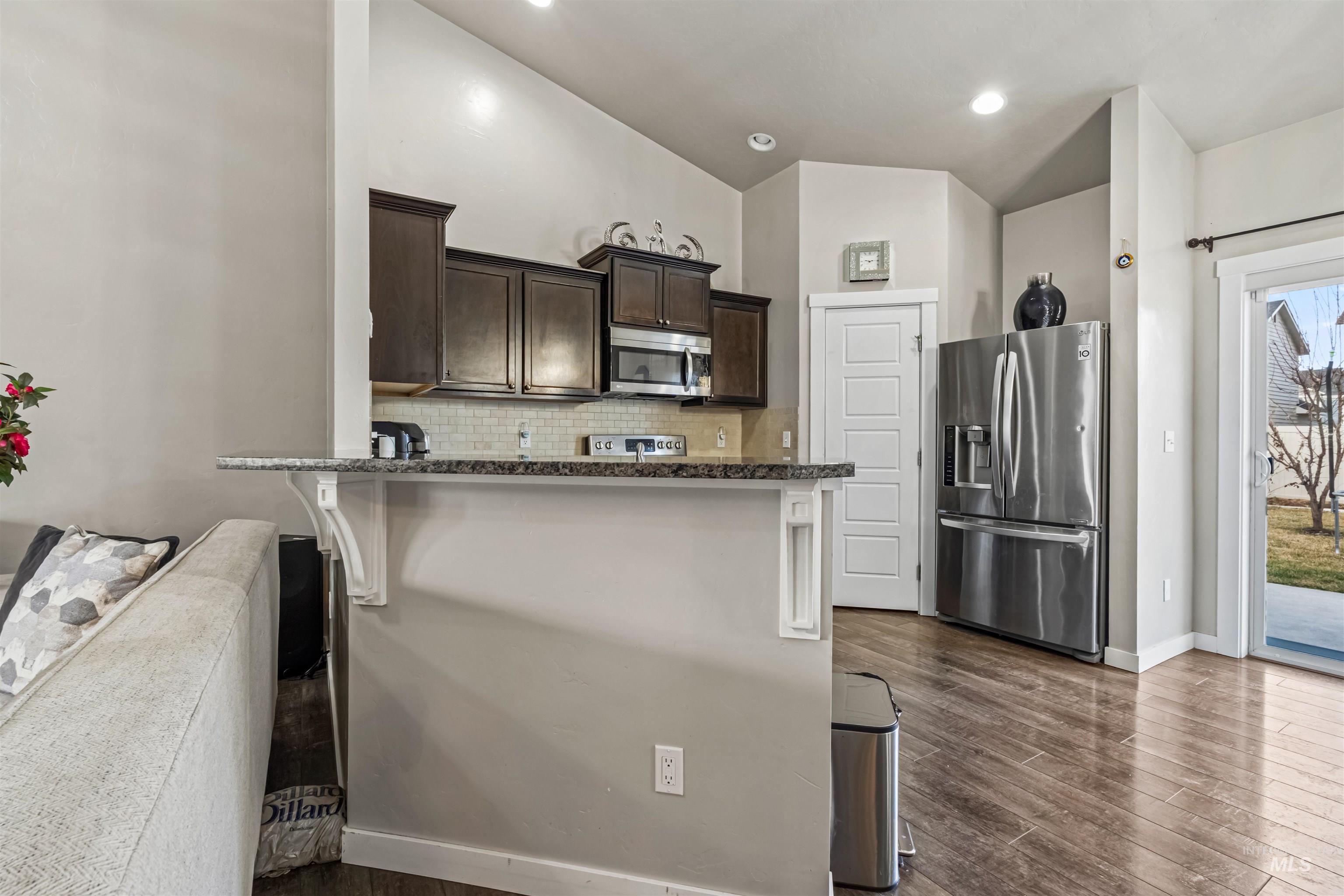12030 West Abram Street Boise, ID 83713 - Photo 7 of 26 Kitchen featuring dark wood finish cabinets, stainless steel appliances, backsplash, dark wood-style flooring, and a breakfast bar area