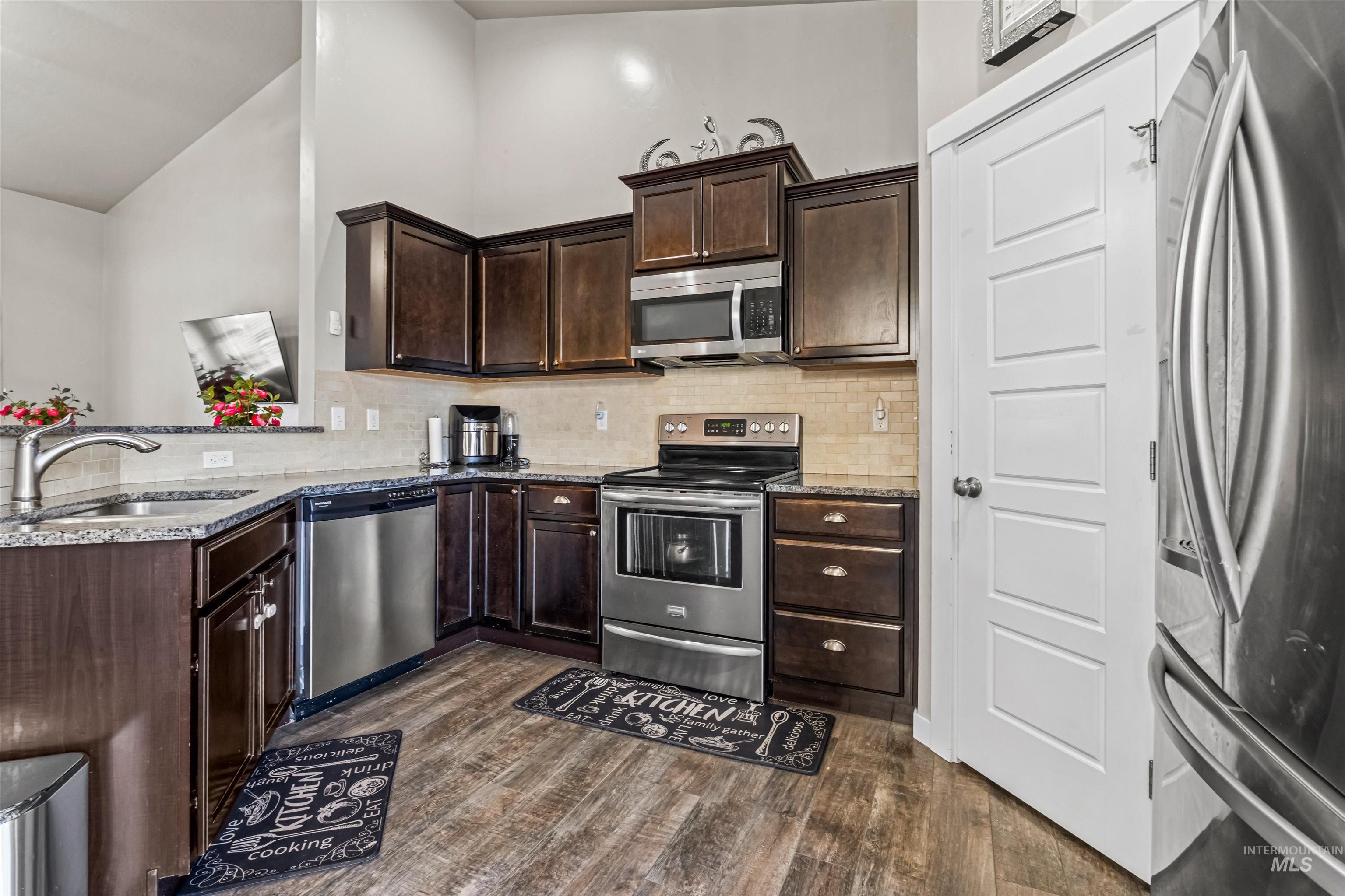 12030 West Abram Street Boise, ID 83713 - Photo 8 of 26 Kitchen with dark wood finish cabinets, stainless steel appliances, light stone countertops, dark wood-style floors, and lofted ceiling