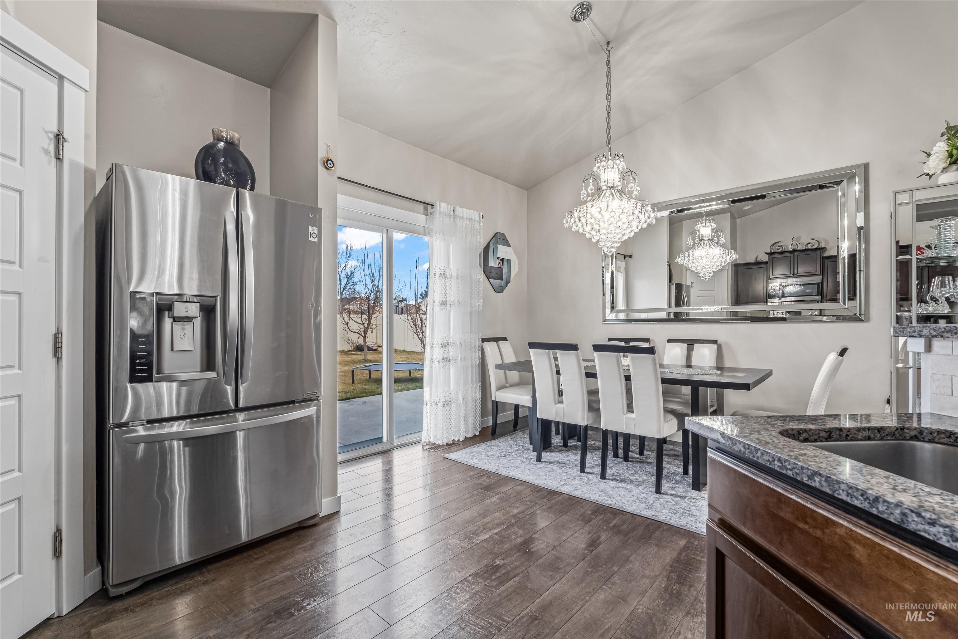 12030 West Abram Street Boise, ID 83713 - Photo 9 of 26 Kitchen with stainless steel fridge, lofted ceiling, dark wood-type flooring, dark wood finish cabinets, and dark stone countertops