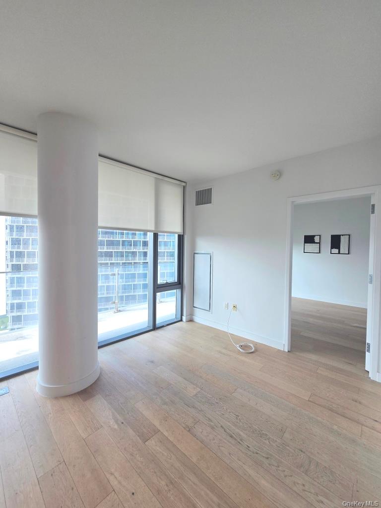 131-01 40 Road, Unit 11P Queens, NY 11354 - Photo 11 of 17 wooden floor in an empty room with a window
