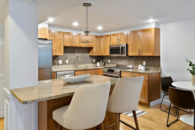 a kitchen with stainless steel appliances granite countertop a stove a sink a microwave refrigerator and chairs