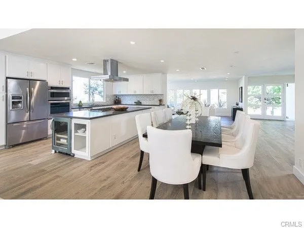 a living room with stainless steel appliances kitchen island granite countertop a dining table chairs and a refrigerator
