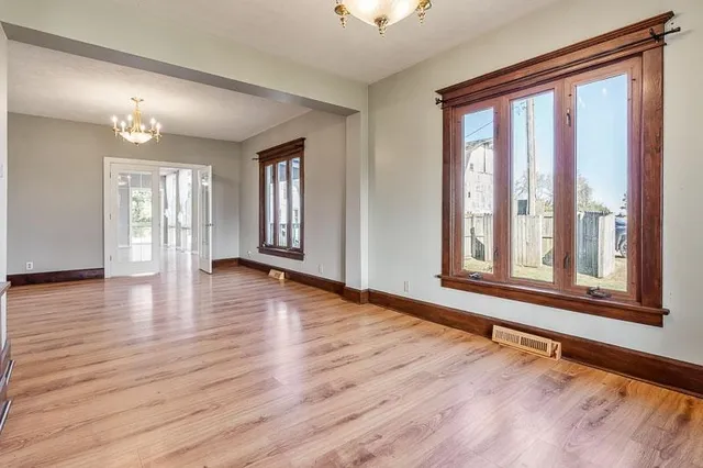 an empty room with wooden floor chandelier and windows