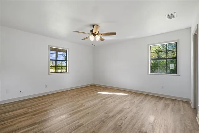 an empty room with wooden floor chandelier fan and windows