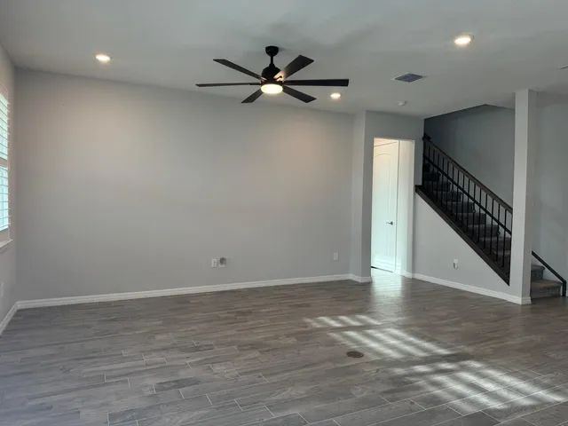 an empty room with wooden floor fan and windows