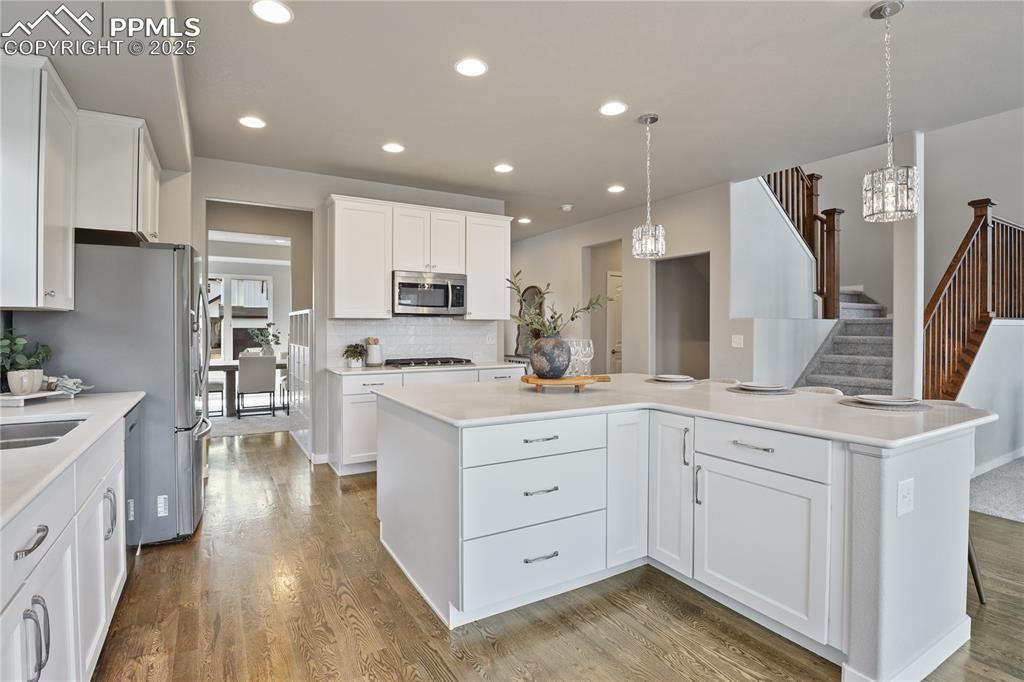 11848 Alydar Loop Colorado Springs, CO 80921 - Photo 10 of 50 Kitchen with stainless steel appliances, a chandelier, wood finished floors, white cabinetry, and recessed lighting