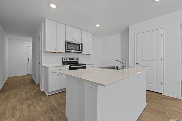 a kitchen with stainless steel appliances a sink a stove a microwave a refrigerator a white cabinets and wooden floor