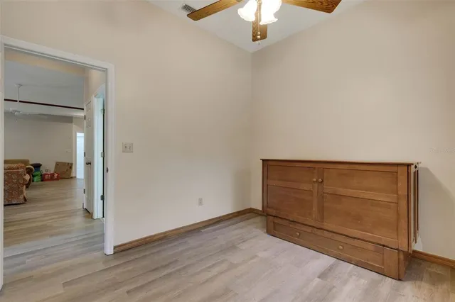 an empty room with wooden floor chandelier fan and windows