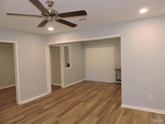 an empty room with wooden floor fan and windows