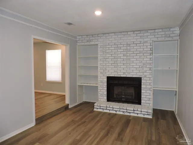a view of an empty room with wooden floor fireplace and a window
