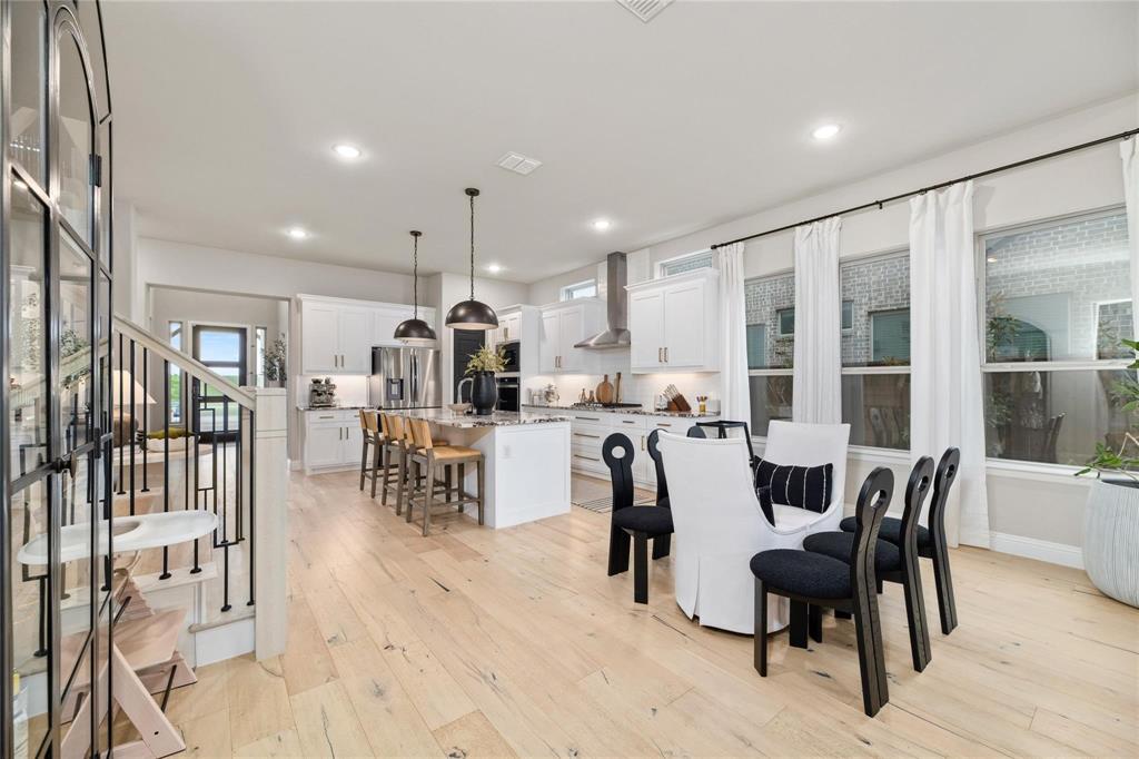 2262 Poppyvine Road Frisco, TX 75033 - Photo 10 of 40 Open-concept kitchen and dining area featuring light wood-finish flooring, a kitchen island with pendant lighting, white cabinetry, and stainless steel appliances