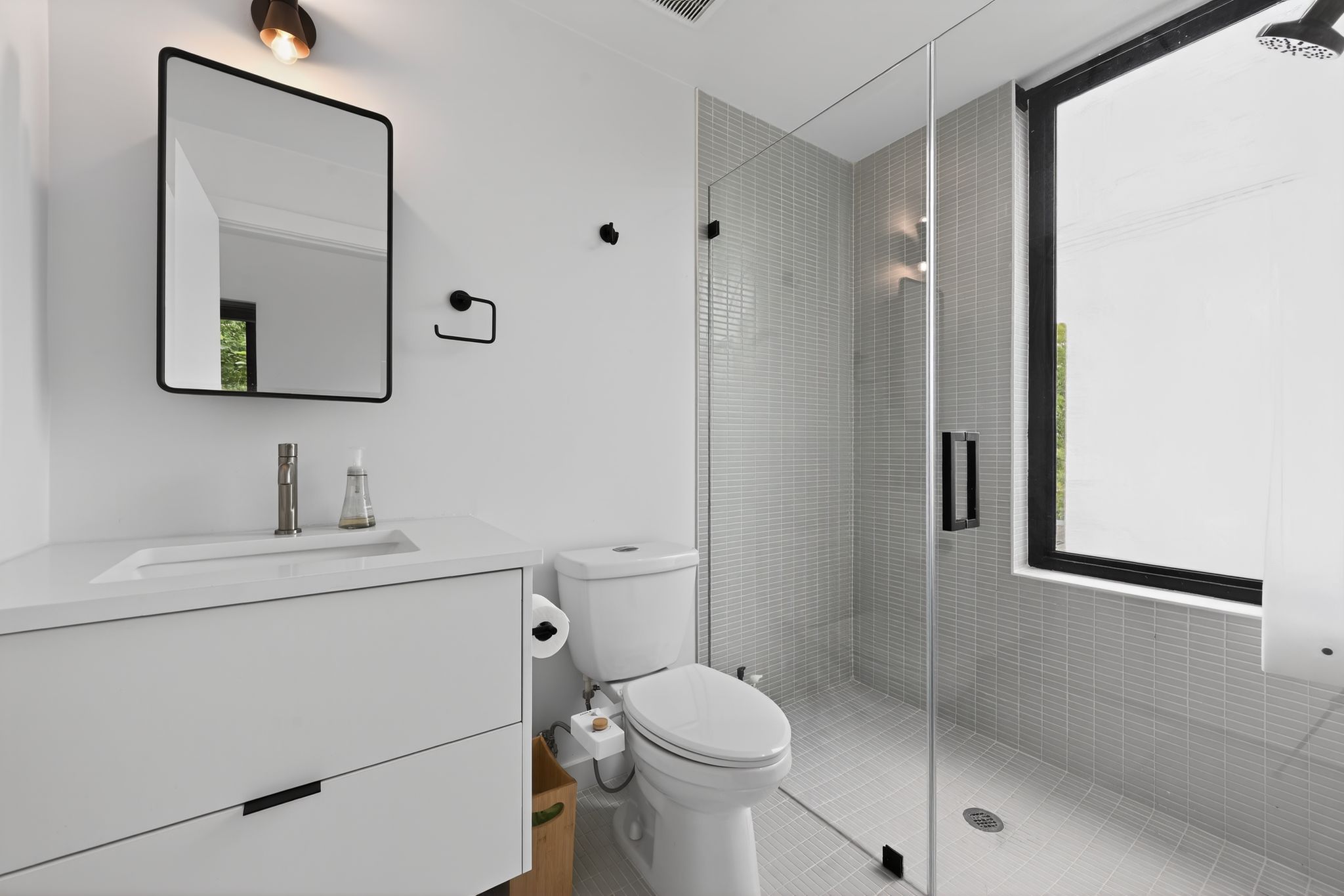 1206 Luna Street, Unit 2 Austin, TX 78721 - Photo 24 of 30 The bathroom features a modern vanity with a white countertop and integrated sink, a frameless glass shower enclosure with gray tile, and a rectangular mirror with a black frame
