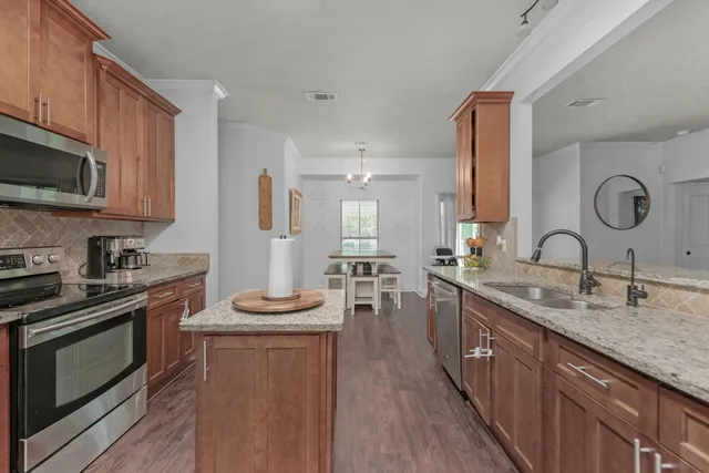 a kitchen with stainless steel appliances granite countertop a stove a sink dishwasher a microwave oven and a dining table with wooden floor