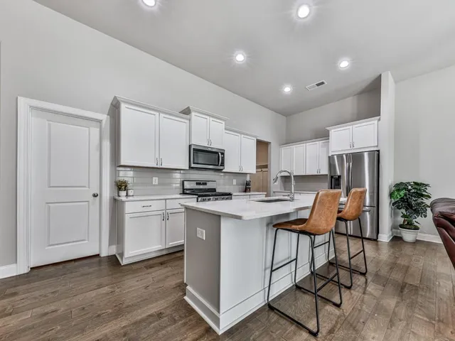 a kitchen with stainless steel appliances kitchen island granite countertop a refrigerator oven a sink a dining table and chairs with wooden floor