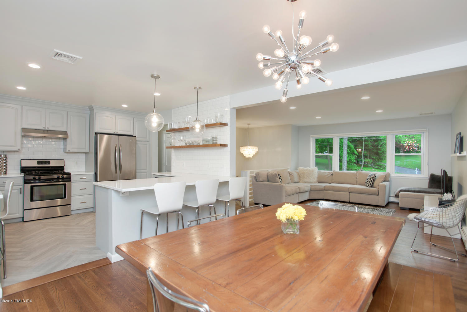 a living room with stainless steel appliances furniture a chandelier and a kitchen view