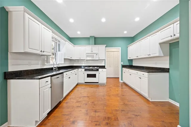 a large kitchen with stainless steel appliances kitchen island granite countertop a stove a sink and white cabinets