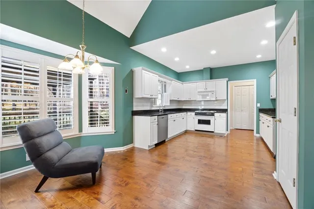 a kitchen with stainless steel appliances kitchen island granite countertop a refrigerator a stove a sink dishwasher and white cabinets with wooden floor