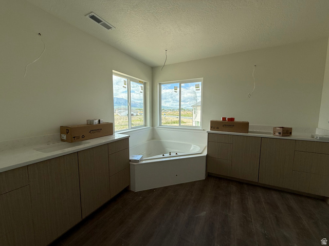 1008 West 3410 South Nibley, UT 84321 - Photo 13 of 26 Spacious bathroom featuring a built-in corner soaking tub, dual window sets, wood-finish flooring, and two elongated vanity cabinets with light-toned countertops