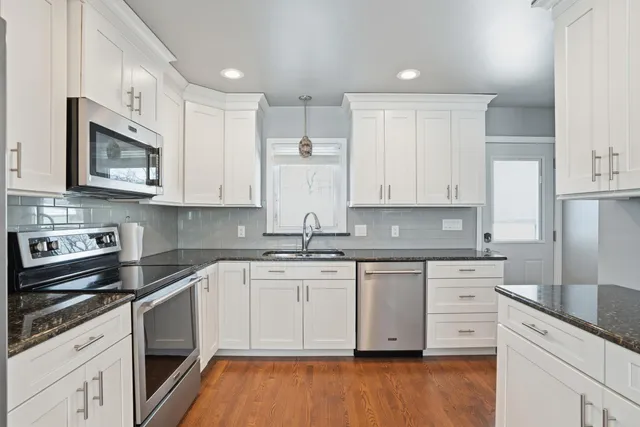 a kitchen with stainless steel appliances granite countertop a stove a sink and white cabinets