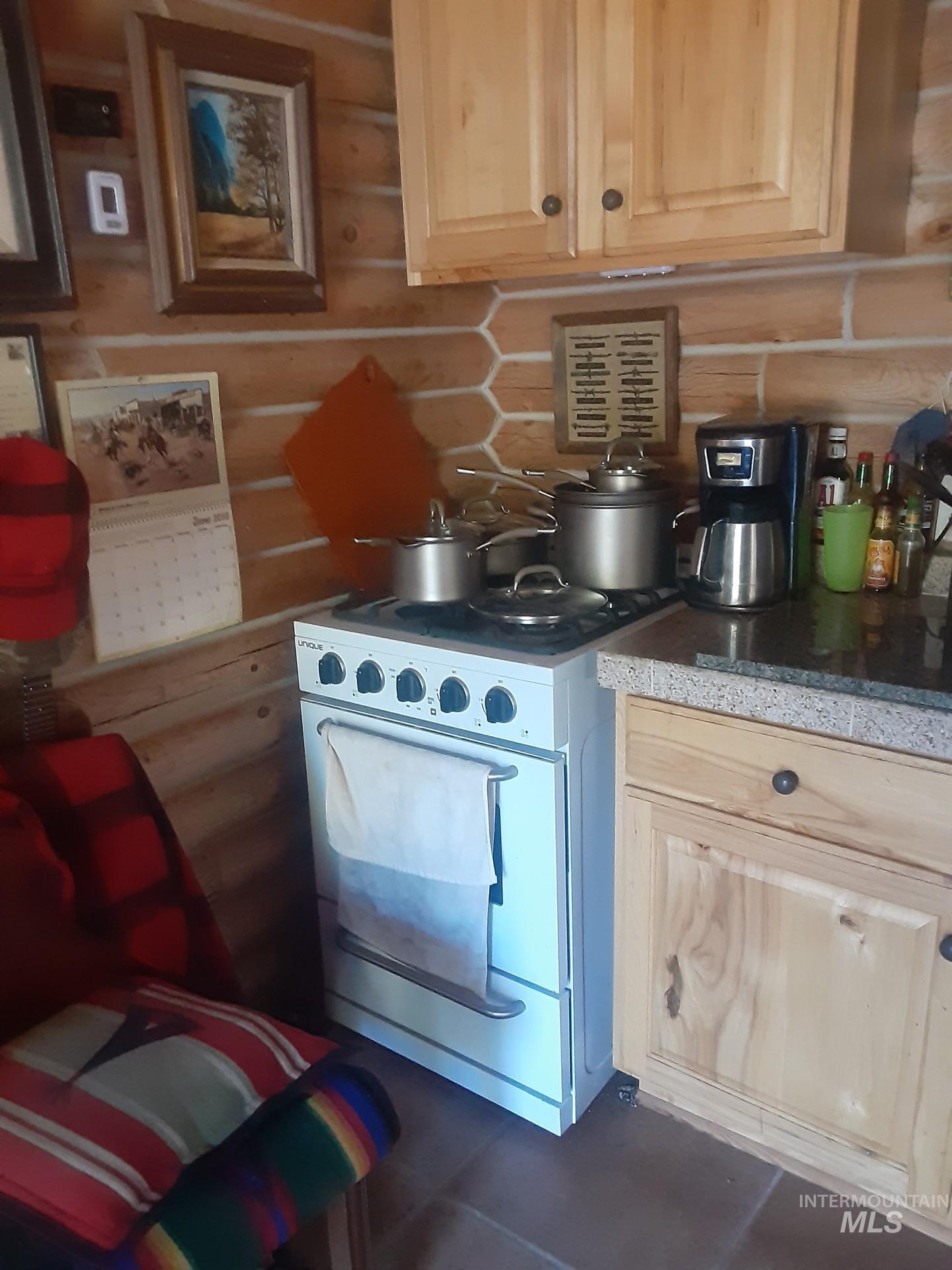 2074 Fleck Smt Road Fairfield, ID 83327 - Photo 12 of 22 Kitchen with light brown cabinetry, white stove, rustic walls, and dark tile patterned flooring