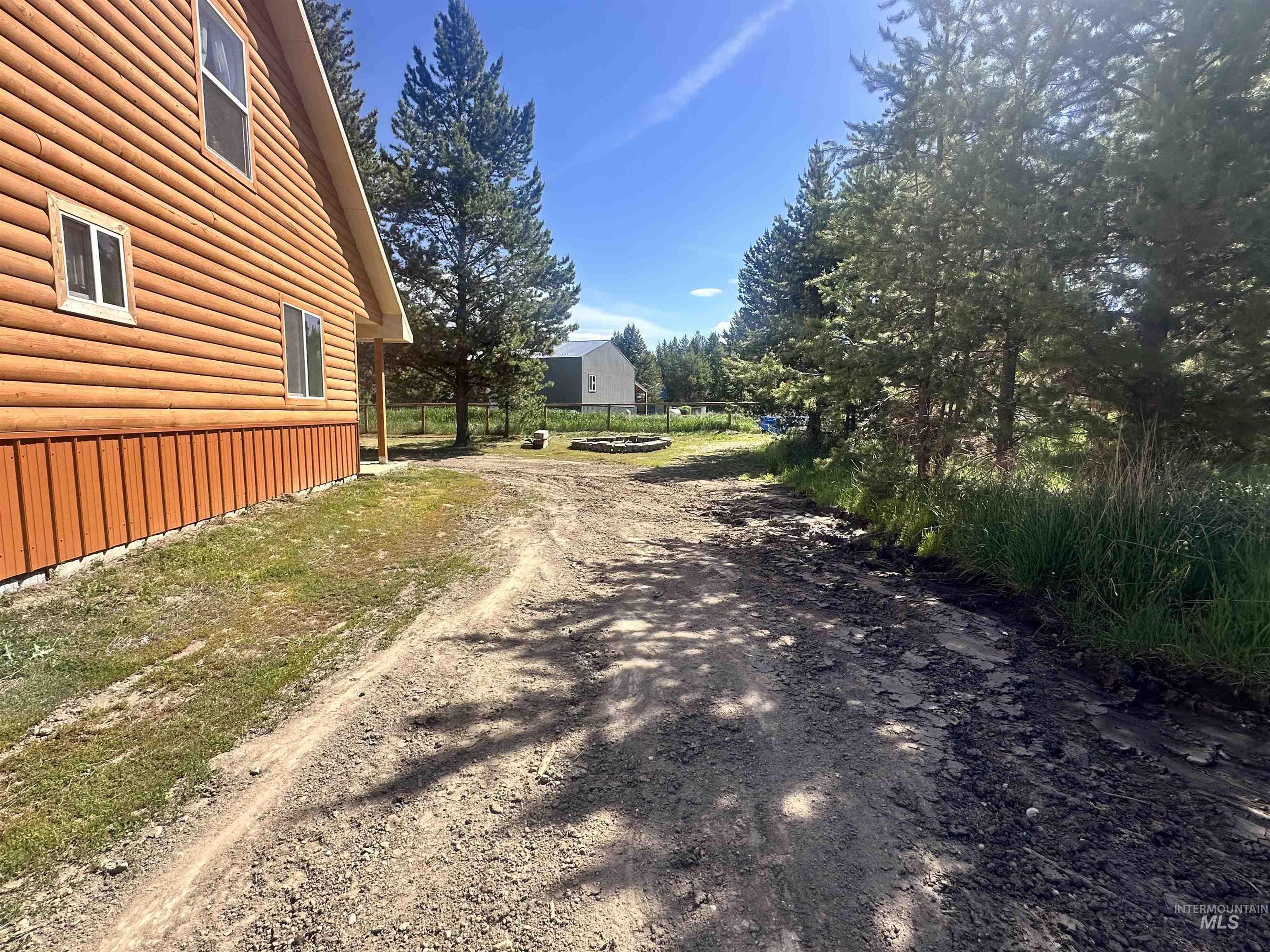 22 West Prospectors Drive Cascade, ID 83611 - Photo 6 of 29 Log-sided exterior with white-framed windows, a gravel driveway, and surrounding mature evergreen trees