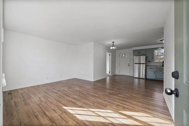 a view of empty room with wooden floor and kitchen