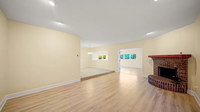 an empty room with wooden floor fireplace and windows