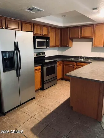 a kitchen with stainless steel appliances granite countertop a refrigerator a stove and a sink with wooden cabinets