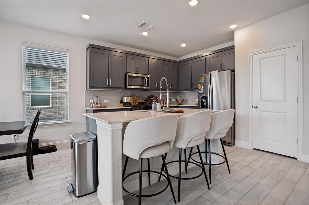 3115 Giovanni Point Princeton, TX 75407 - Photo 10 of 26 Modern kitchen featuring an island with a breakfast bar, gray cabinetry, stainless steel appliances, and light-toned tile flooring
